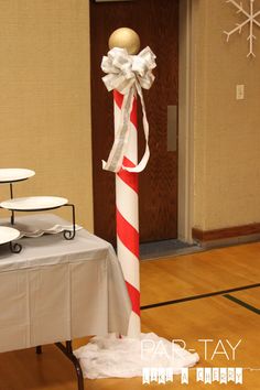 a tall candy cane decorated with white and red ribbon on top of a wooden floor