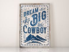 a sign that says dream big little cowboy on the side of a wall with mountains in the background