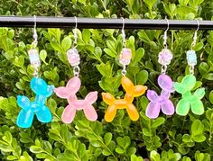 four different colored plastic flowers are hanging from a wire in front of some green bushes