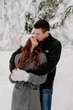 a man and woman kissing in front of snow covered pine trees on a snowy day