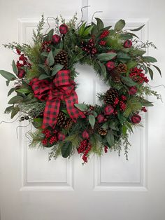 a christmas wreath with pine cones, berries and greenery hanging on a white door