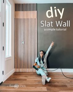 a woman is sitting on the floor in front of a sign that says diy slat wall