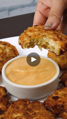 a person dipping something into a small white bowl on top of a plate with fried food