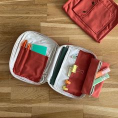 an open suitcase sitting on top of a wooden floor next to a bag with pens and pencils in it