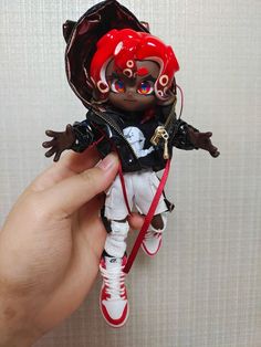 a hand holding a toy doll with red hair and makeup on it's face