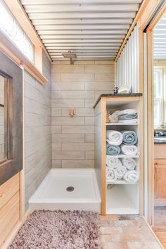 a bathroom with wooden walls and flooring has white towels on shelves next to the shower