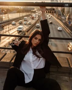 a woman sitting on top of a metal rail next to a street filled with traffic