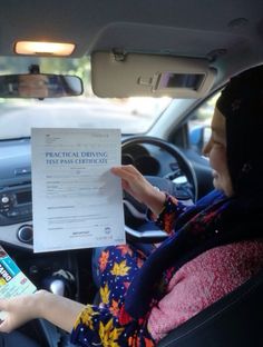 a woman sitting in the driver's seat of a car holding up a driving test paper