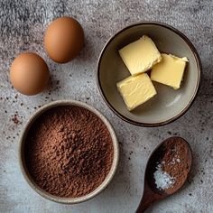 three bowls with chocolate, butter and eggs next to each other on a gray surface