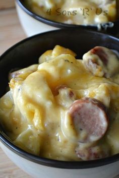 two bowls filled with macaroni and cheese covered in sausages on top of a wooden table