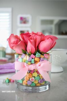 pink roses are in a glass vase filled with candy and marshmallow candies