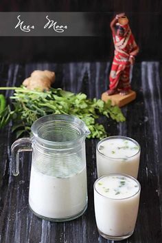 two glasses of milk sitting on top of a wooden table next to some vegetables and a statue