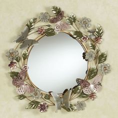 a decorative mirror with flowers and butterflies around the edges, hanging on a beige wall