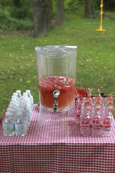 a red and white checkered table cloth with cups on it, water bottles in the background