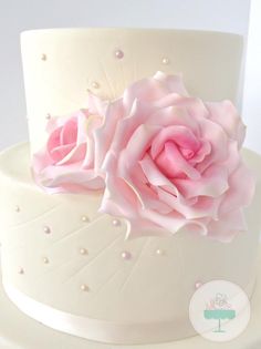 a three layer white cake with pink flowers on the top and pearls around the edges