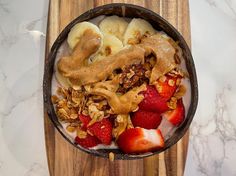 a bowl filled with yogurt, granola and strawberries on top of a wooden cutting board