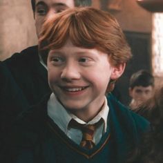 a boy with red hair is smiling and wearing a harry potter outfit in front of other people