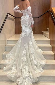 a woman in a white wedding dress standing on stairs with her back to the camera