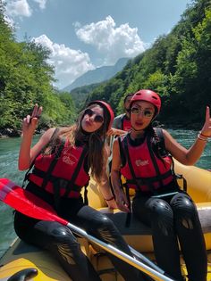 two women in life jackets and helmets are on a raft with their arms up as they float down the river