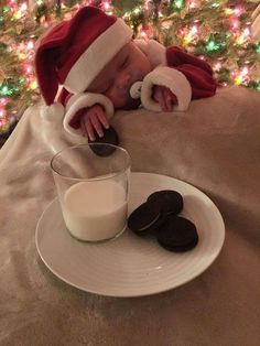 a baby in a santa hat is sleeping next to cookies and milk