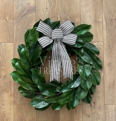 a green wreath with a bow on top of it sitting on a wooden floor next to a wall