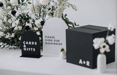 three black and white gift boxes sitting on top of a table with flowers in the background