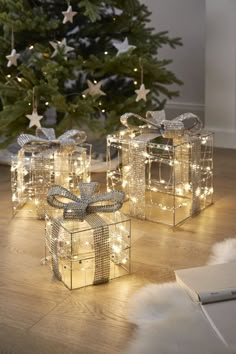 two presents wrapped in silver ribbon with lights on them sitting next to a christmas tree