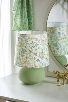 a green lamp shade sitting on top of a white table next to a mirror and toy giraffe