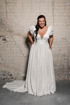 a woman standing in front of a brick wall wearing a white dress with puffy sleeves