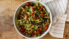 a white bowl filled with zucchini, tomatoes and other veggies on top of a wooden table