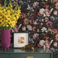 a vase filled with yellow flowers sitting on top of a green dresser next to a wall