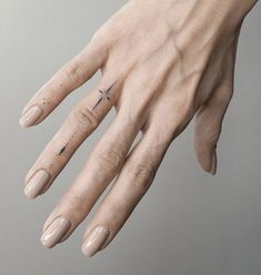 a woman's hand with a tiny cross tattoo on it, and the ring finger