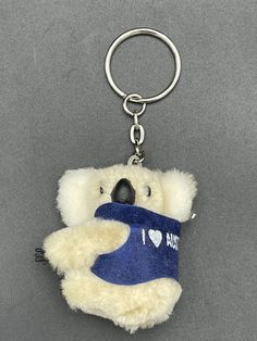 a white teddy bear with a blue t - shirt on it's chest is holding a keychain