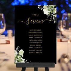 a table sign sitting on top of a wooden easel next to wine glasses and candles