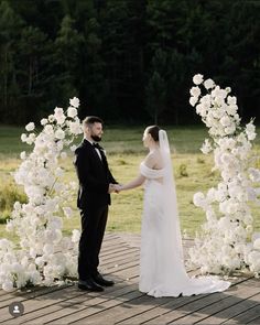 a bride and groom standing next to each other in front of a flower covered arch