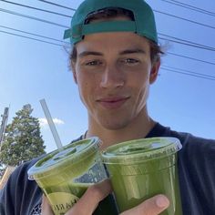 a young man holding two cups of green smoothie