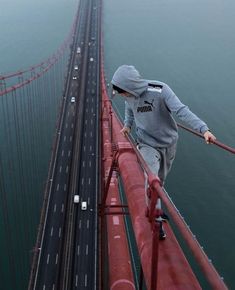 a man is walking across the bridge on his skateboard while wearing a hoodie