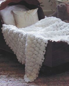 a white crocheted blanket on top of a bed next to pillows and blankets