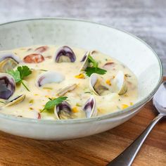 a bowl of clam chowee on a cutting board with a spoon and fork