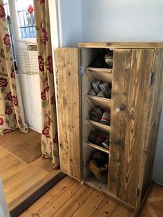 a wooden cabinet with shoes inside of it on the floor in front of a door