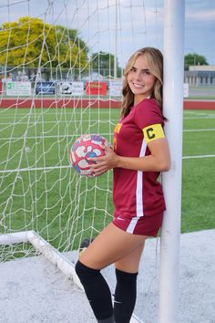 a girl posing with a soccer ball in front of a goal