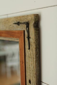 a mirror hanging on the wall with a wooden frame and metal hook attached to it