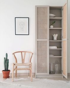 an empty chair sits in front of a white bookcase with two plants on it