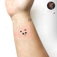 a small panda bear tattoo on the left inner arm and wrist, with black eyes