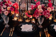 the table is set with black and gold place settings, pink flowers, candles, and napkins