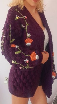 a woman wearing a purple knitted cardigan with flowers and leaves on the front