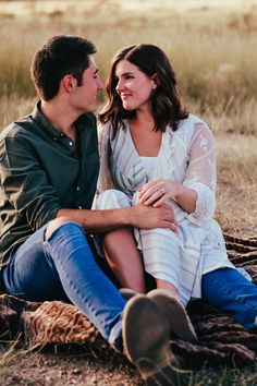 a man and woman are sitting on a blanket in the grass together, looking into each others eyes