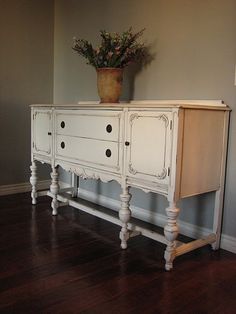 a white dresser sitting on top of a hard wood floor next to a vase with flowers