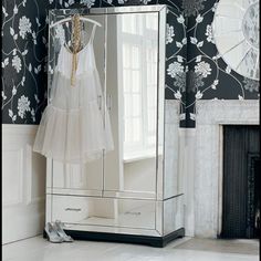 a white dress hanging on a mirror in front of a wall with black and white flowers