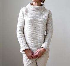 an older woman standing with her hands in her pockets and wearing a white turtle neck sweater